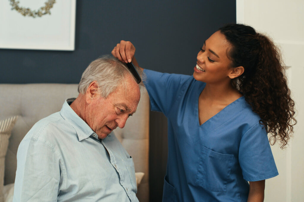 Home health care franchise - Shot of a young nurse helping her senior patient get ready in the morning at home by brushing his hair