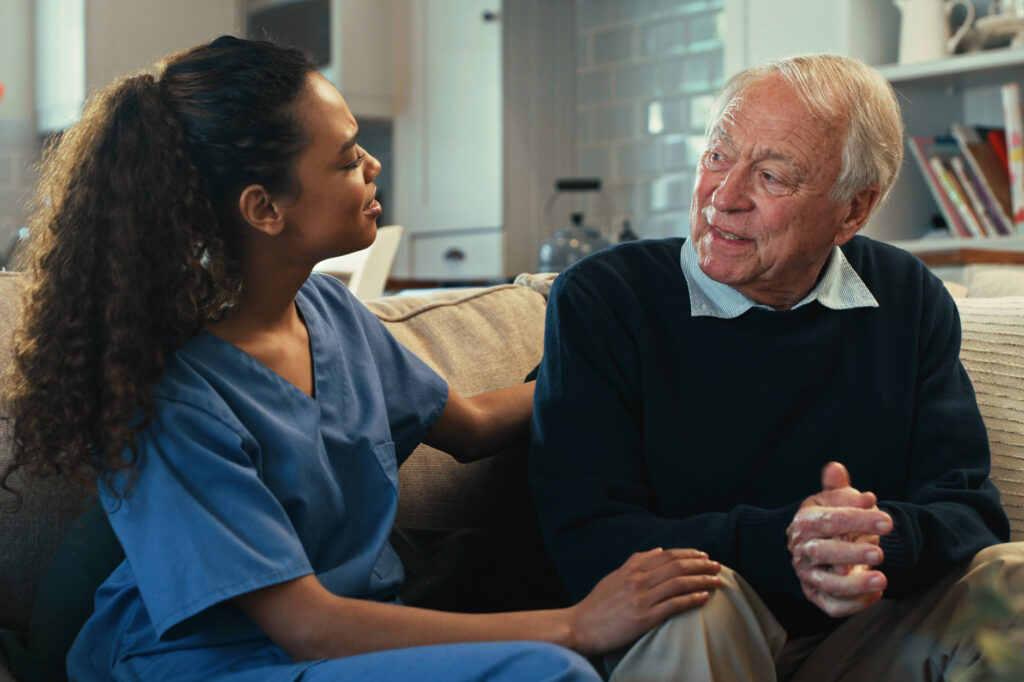 Home health care franchise - Shot of a young nurse sitting with her senior patient on the sofa at home and comforting him